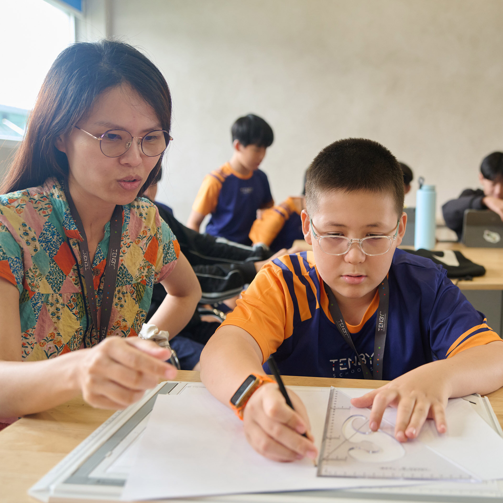 Student drawing lines with the help of his teacher