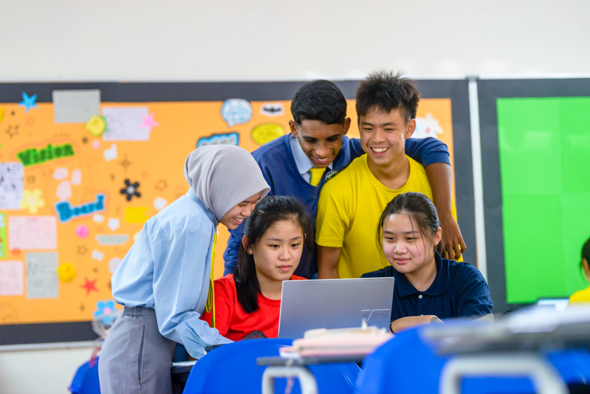 Teenagers smiling while looking at a laptop screen